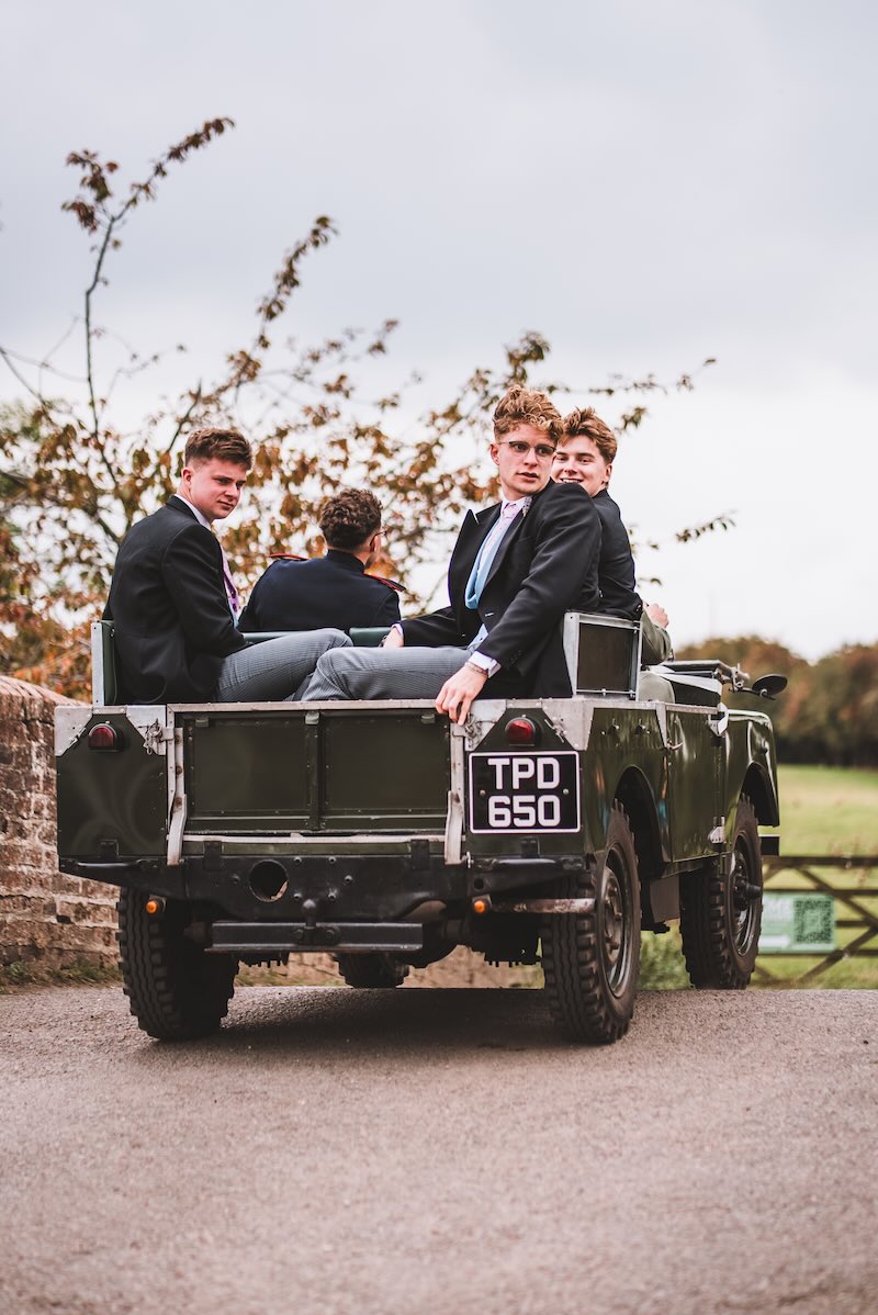 A vintage Land Rover transporting the groom and groomsmen across a Berkshire estate, captured in a documentary style.