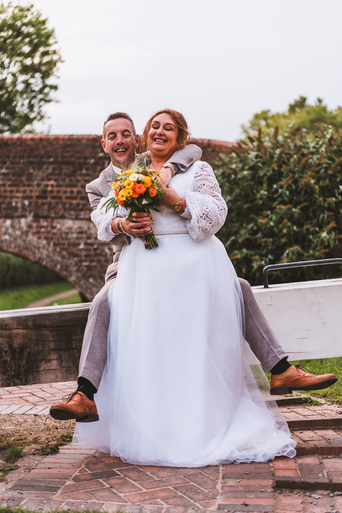 A documentary wedding photograph of a bride and groom sitting on a lock gate at Braunston Marina.