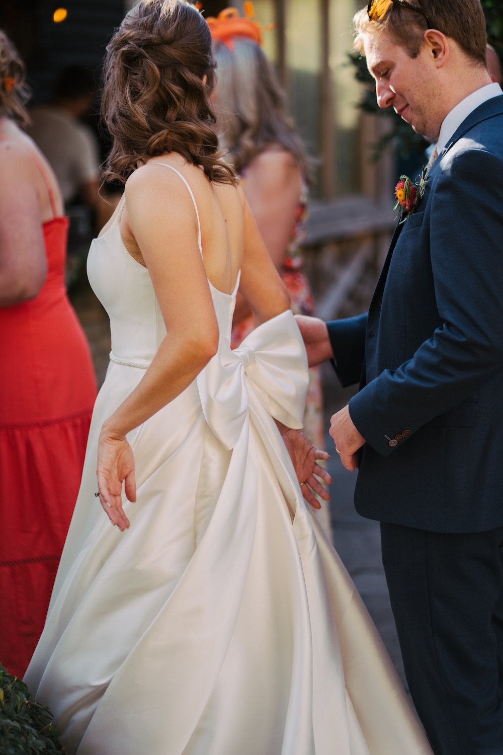 A groom helps adjust the bow on his bride's dress in golden evening light during a London wedding, captured in documentary style.