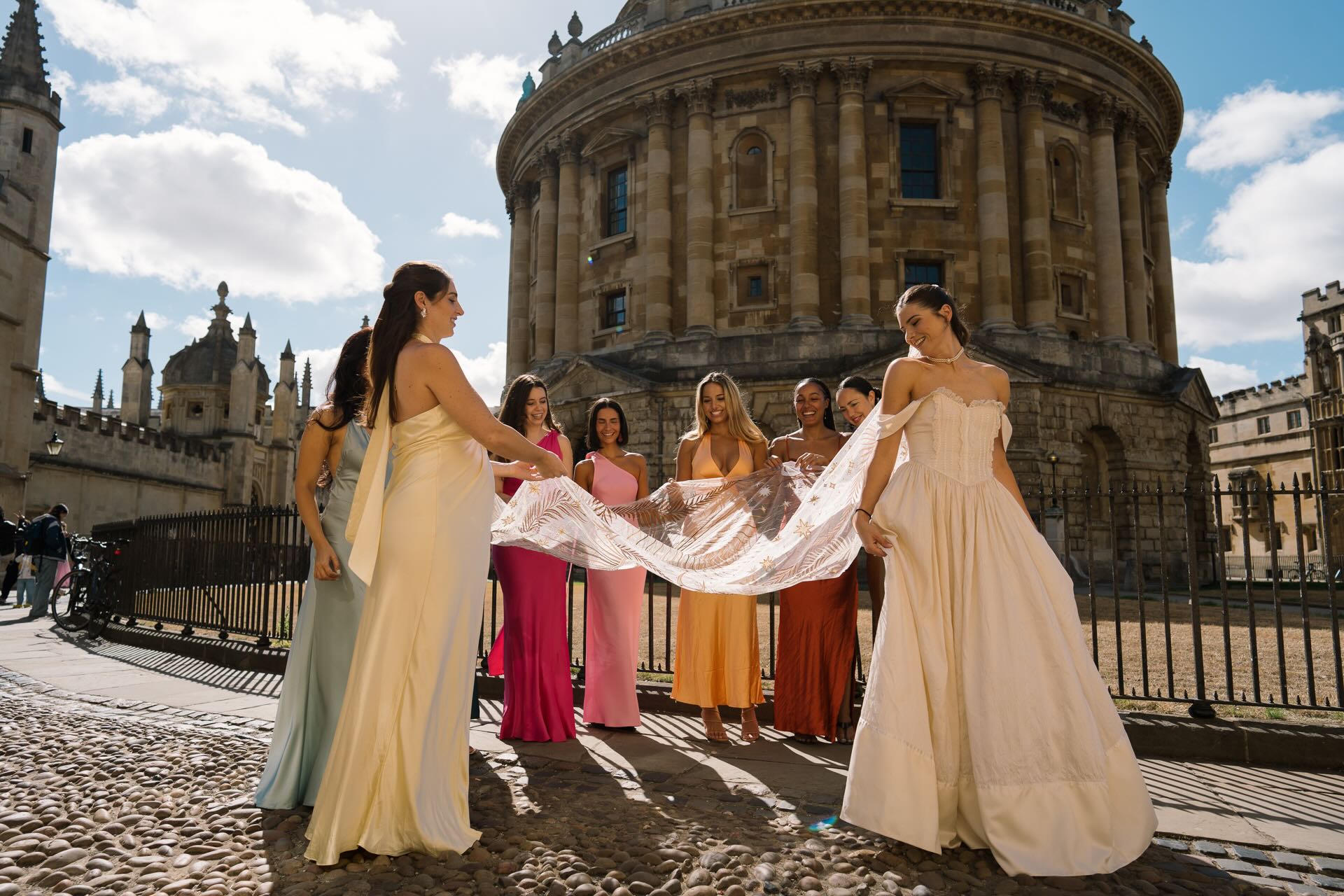 Bride and bridesmaids holding a veil near the Radcliffe Camera during unposed wedding photography and films