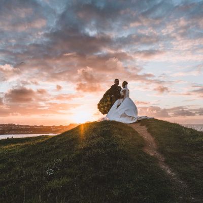 A cinematic documentary wedding photograph of a bride and groom at sunset overlooking the Newquay Bay coastline in Cornwall.