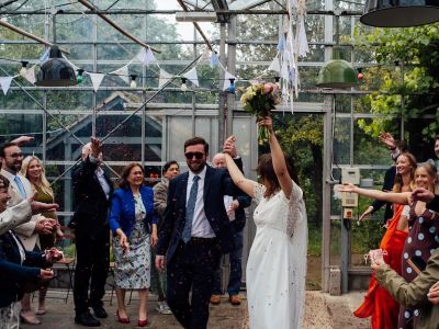 Roo and Rob walking through confetti inside the greenhouse at Worton Kitchen Garden